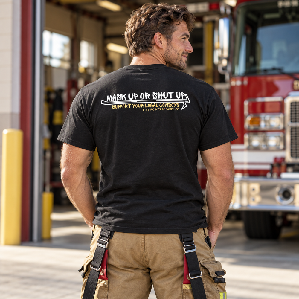Firefighter wearing the black First Due Not First Rodeo shirt beside a firehouse bay.