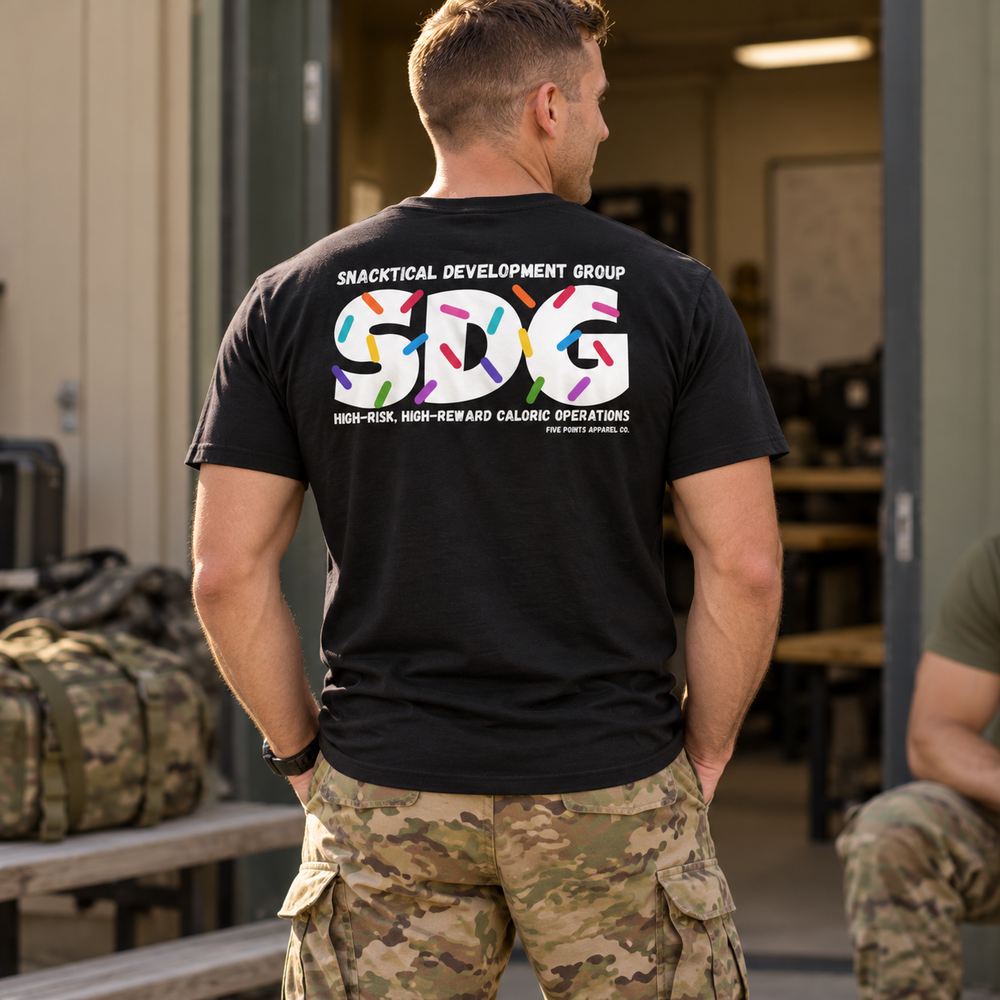 Service member wearing the black SNACKTICIAN MIL shirt outside a team room.